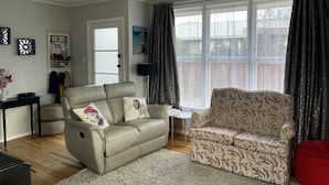 A living room with a beige sofa, patterned armchair, and a small side table. A door with a glass panel and a Wi-Fi sign is visible. - Take time out in Turangi - family friendly (Turangi)