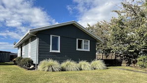 A single-story house with a dark siding exterior, two windows with white trim, and a satellite dish on the roof. - Take time out in Turangi - family friendly (Turangi)