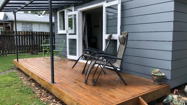 A wooden deck with outdoor furniture, a covered patio, and a house with grey siding. - Take time out in Turangi - family friendly (Turangi)