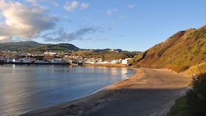 A coastal town with a sandy beach, a calm sea, and a backdrop of hills and buildings. - Internacional Azores Boutique (Horta)