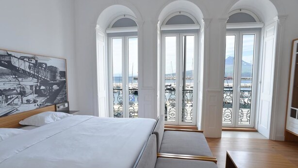 A hotel room with a large bed, a view of the harbor, and arched windows. - Internacional Azores Boutique (Horta)