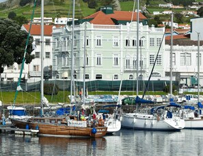 Un puerto deportivo con varias embarcaciones amarradas, un edificio grande con techo rojo y una ladera cubierta de hierba al fondo.