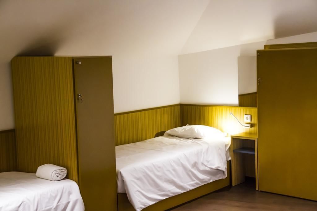 A small, single-room hotel room with a bed, a nightstand, and a wardrobe.