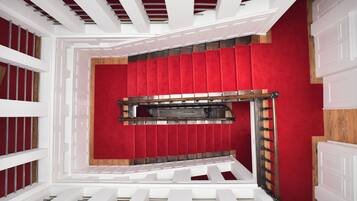 Una escalera con un muro cubierto de alfombra roja, barandillas blancas y un pasamanos de madera.