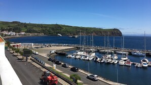 A marina with boats docked, a road with vehicles, and a hilly landscape in the background. - Internacional Azores Boutique (Horta)