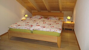 Een slaapkamer met een houten plafond, een bed met bloemenbeddels, twee nachtkastjes met lampen, en een houten vloer.