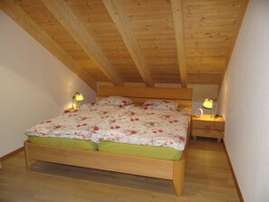 Une chambre avec un plafond en bois, un lit recouvert d’une literie à motifs floraux, deux tables de chevet avec des lampes et un plancher en bois.
