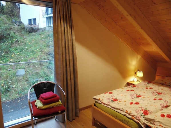 A bedroom with a bed, a chair, a nightstand, and a window with curtains.