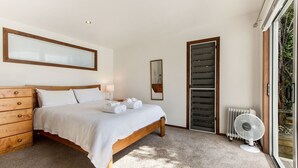 Un dormitorio con cama de madera, cómoda, espejo, radiador y ventana con vistas a la vegetación.