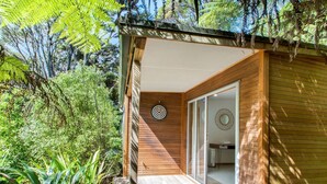 Una cabaña de madera con puerta de cristal que da a un baño, rodeada de exuberante vegetación.