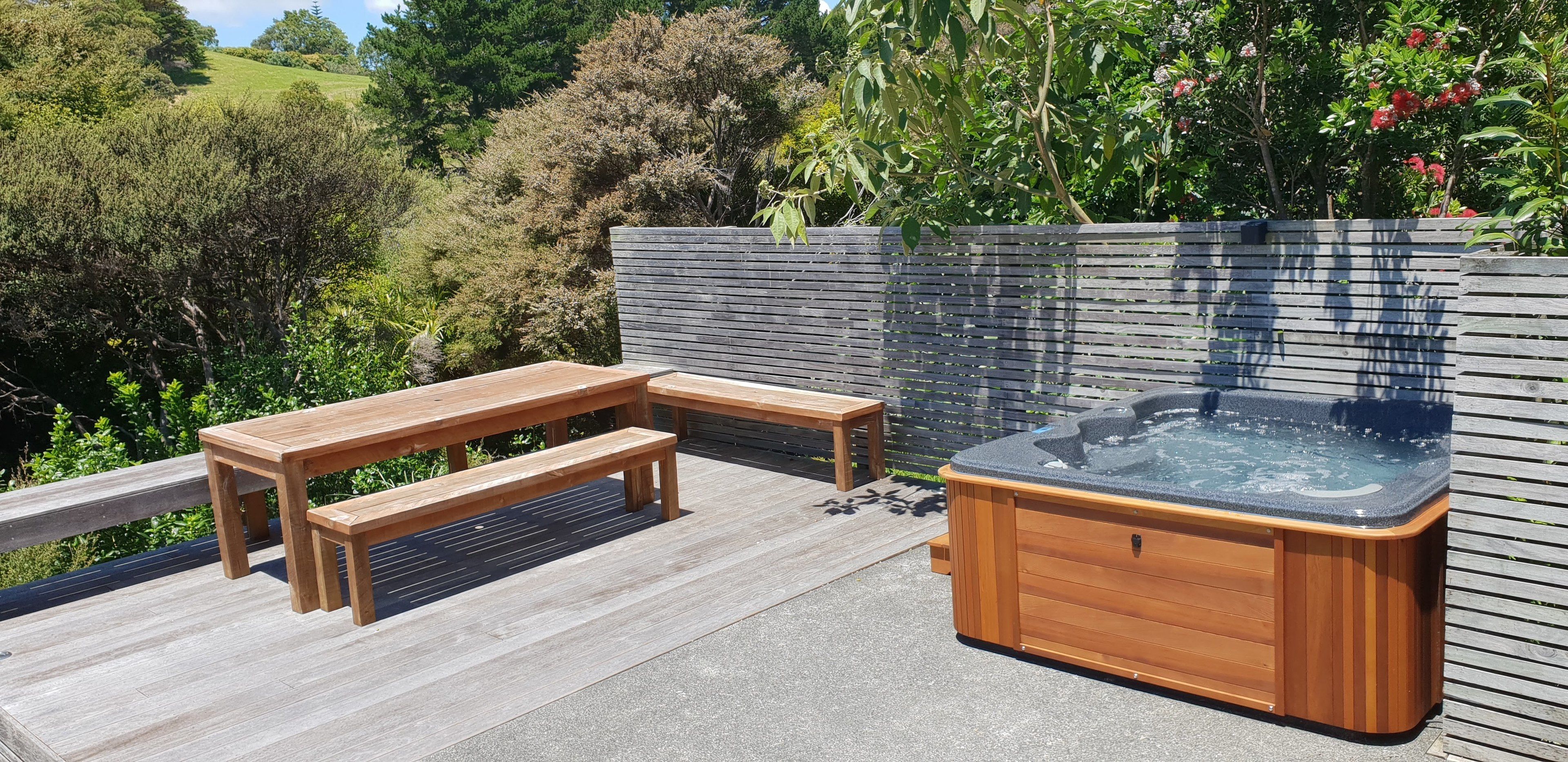A wooden deck with a hot tub and picnic table, surrounded by a wooden fence and lush greenery.