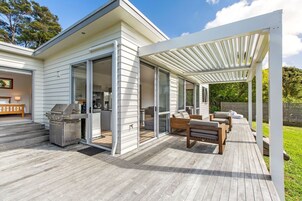 Una casa moderna con un patio cubierto, una parrilla y una zona de comedor con mobiliario exterior.