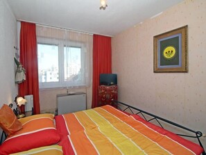 A bedroom with a bed, a radiator, a television on a cabinet, and a window with red curtains. - Vienna waits for you by Interhome (Vienna / 5. District)