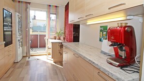 A modern kitchen with wooden cabinets, a red coffee machine, and a view of the outside balcony. - Vienna waits for you by Interhome (Vienna / 5. District)
