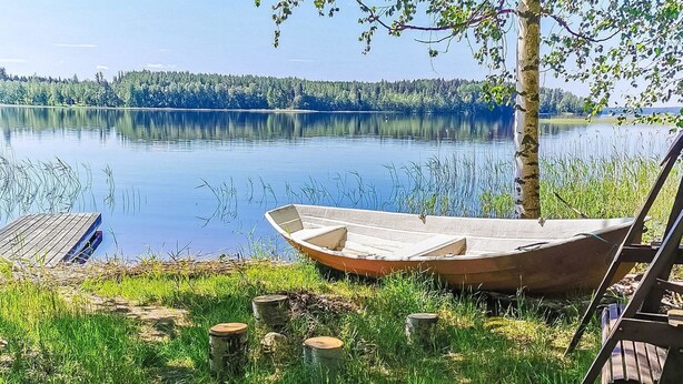 Un bote de madera en un lago tranquilo con un muelle y un árbol en primer plano.