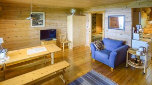 Interior de una cabaña de madera con televisor, muebles de madera, un sofá y una zona de cocina.