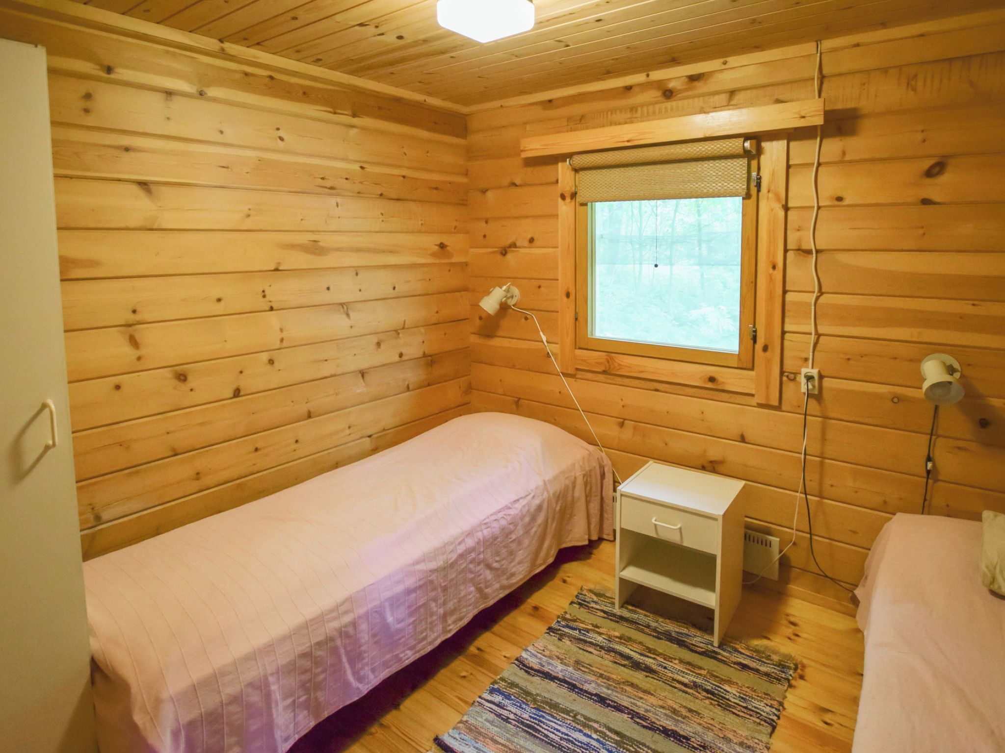 A small, wooden cabin room with a single bed, a nightstand, a window, and a power outlet.