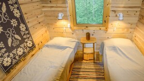 Acogedora habitación tipo cabaña con dos camas, una mesita y una ventana con vistas al bosque.