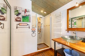 A bathroom with a glass bowl sink, wooden floor, and a shower with a wooden door.