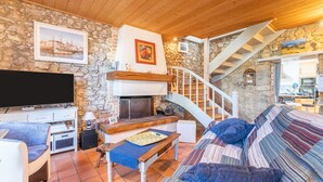 Una sala de estar acogedora con pared de piedra, chimenea, sofá, televisor y escalera.
