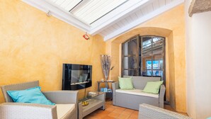 Una habitación iluminada por el sol con muebles de mimbre, un televisor de pantalla plana y un ventanal grande.