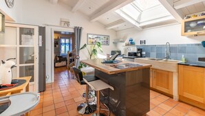 Una cocina moderna con una isla central, un comedor con mesa y sillas, y vistas al salón a través de una puerta abierta.