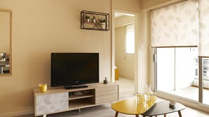 Una habitación de hotel moderna con una televisión de pantalla plana, una mesa consola de madera, un pequeño comedor y un ventanal con vistas.