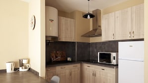 Una cocina compacta con armarios de madera, microondas, refrigerador, cafetera y lavamanos.