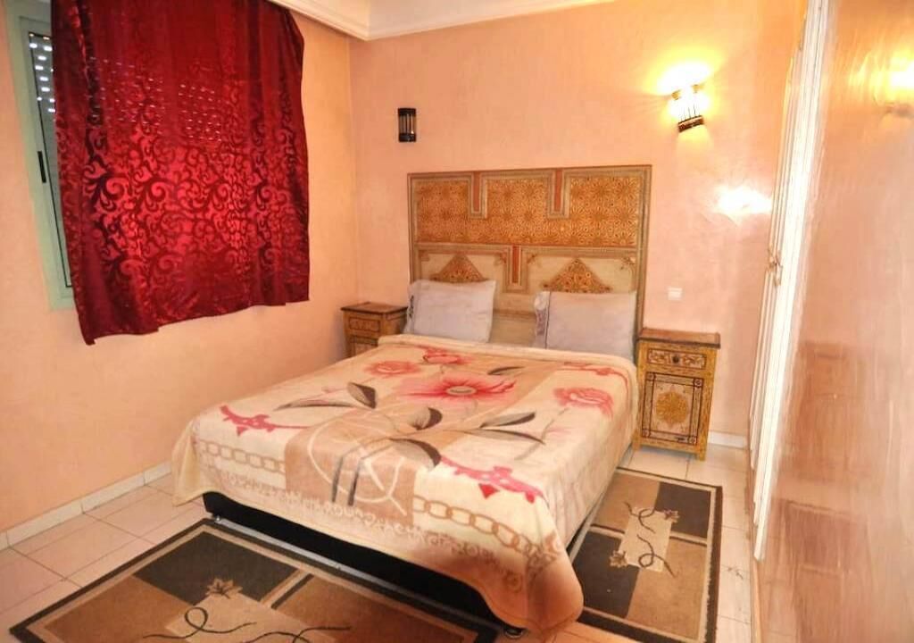 A bedroom with a bed, nightstands, a decorative headboard, and a patterned rug.
