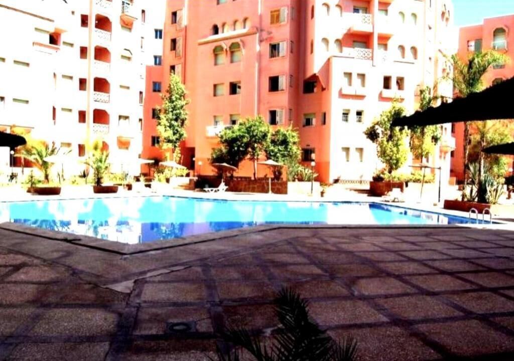 A swimming pool surrounded by potted plants and a multi-story building with balconies.