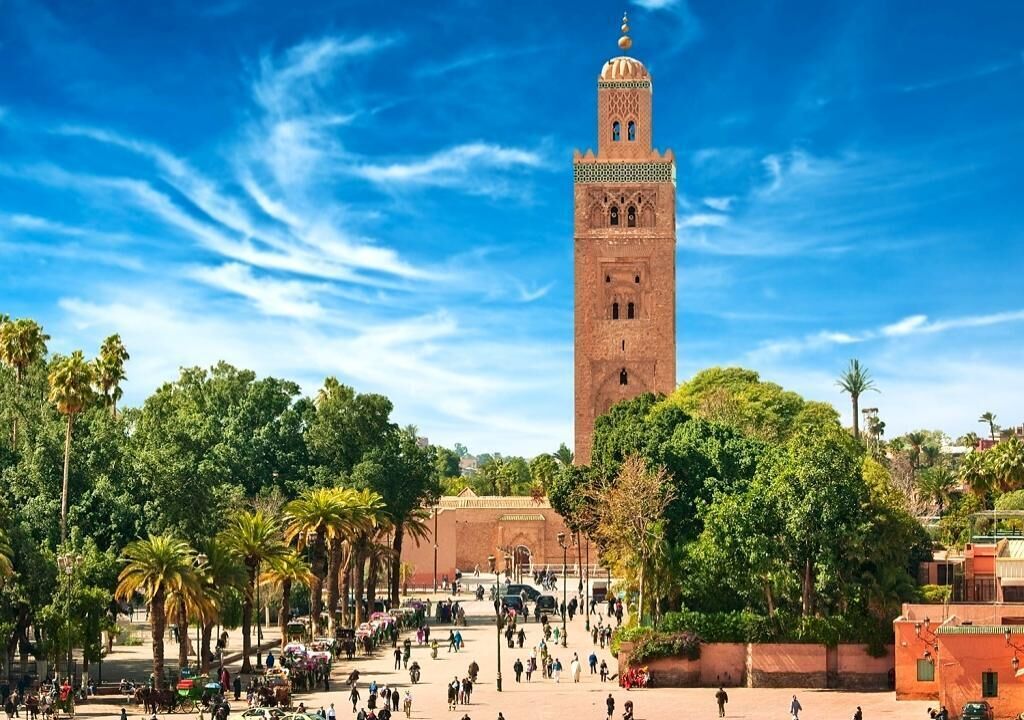 A historic tower with intricate architecture, surrounded by palm trees and a bustling square.