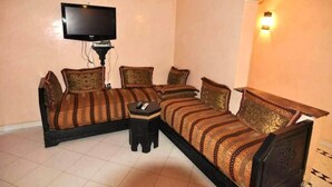 A room with a sofa bed, a small table, a television, and a wall-mounted light fixture. - Residence Atlas Marrakech 3542 (Marrakech)