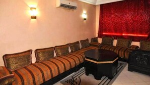 A room with a long sofa set, a small table, and a red patterned wall. - Residence Atlas Marrakech 3542 (Marrakech)