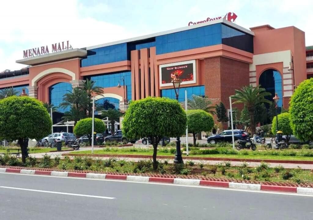 A modern shopping mall with a prominent 'Menara Mall' sign, a 'New Burger' advertisement, and well-maintained landscaping.