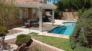 Un patio trasero con piscina, mobiliario de exterior y una pérgola.