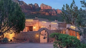 A rustic building with a brick facade, a large arched entrance, and a view of red rock formations in the background.