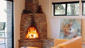 A brick fireplace with a Buddha statue, a modern abstract painting, and a view of trees through the window.