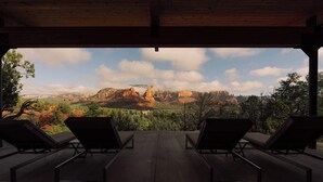 A covered outdoor area with lounge chairs facing a mountainous landscape.