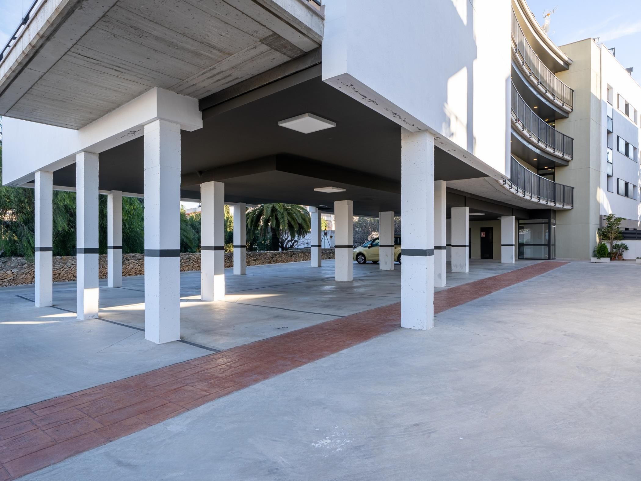 Un área de estacionamiento techada con pilares blancos y un camino de ladrillo rojo.