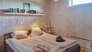 Een slaapkamer met een houten bed, twee kussens, een opgevouwen handdoek en een plank met boeken en een lijst.
