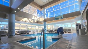 Une piscine intérieure dotée d’un plafond en verre transparent, de chaises longues et d’un panneau de signalisation indiquant clairement la sortie.