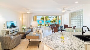 A modern hotel room with a TV, seating area, dining space, and a view of the ocean.