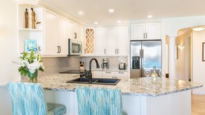 A modern kitchen with white cabinets, a granite countertop, a stainless steel refrigerator, and a built-in microwave.