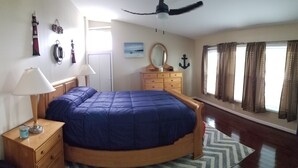Une chambre à coucher comprenant un lit, une table de chevet en bois, une commode et un ventilateur de plafond.