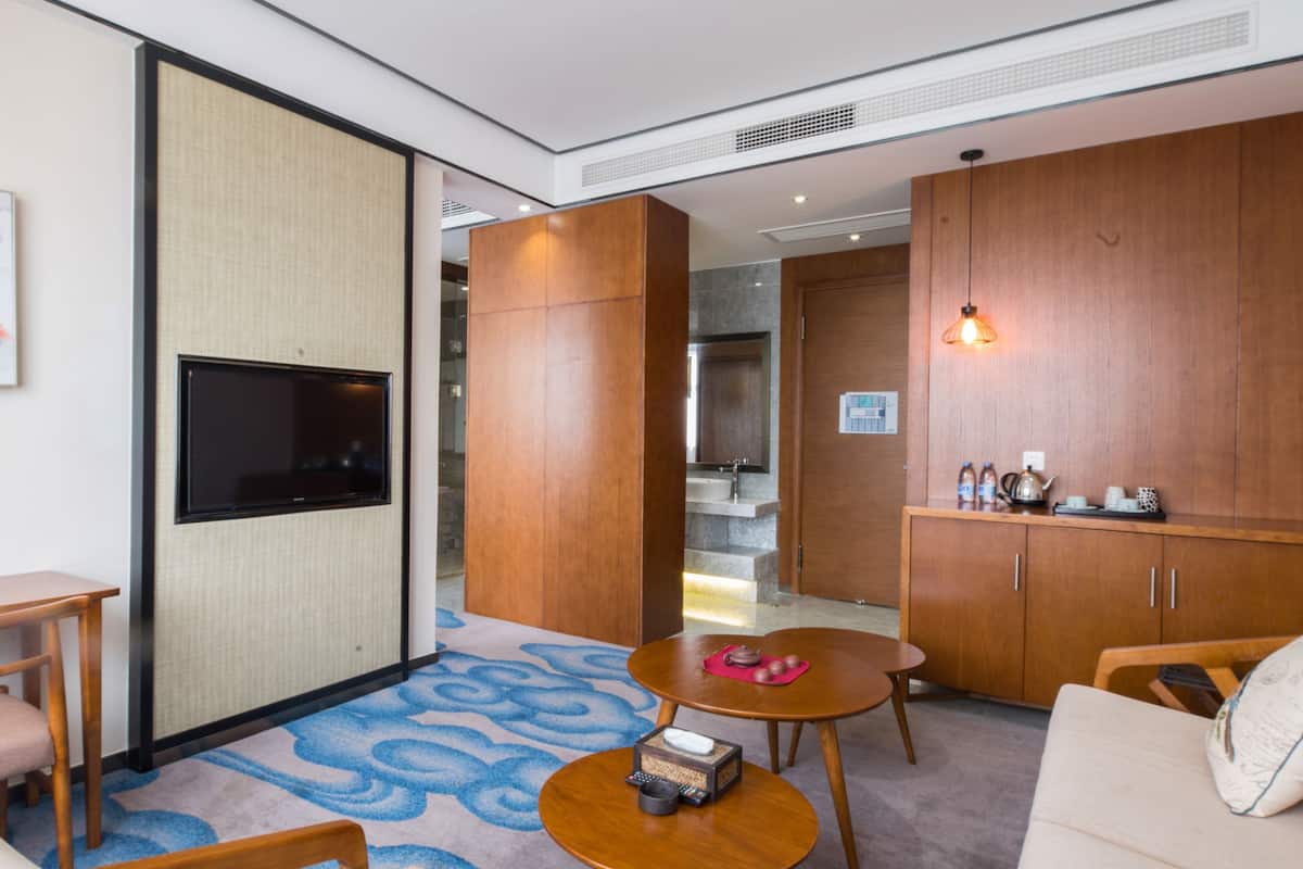 A hotel room with a TV mounted on a wall, a wooden cabinet, a small table with a remote control, and a sofa.