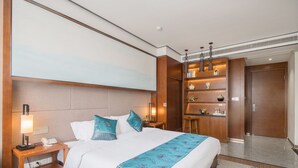 Hotellihuone, jossa on suuri sänky, yöpöytä lampun kanssa, työpöytä tietokoneella ja vaatekaappi.