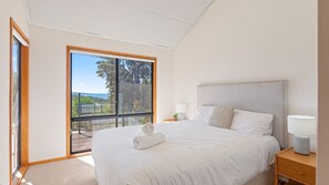 Ein Schlafzimmer mit einem großen Bett, einem Nachttisch, einer Lampe und Blick durch eine Glastür.