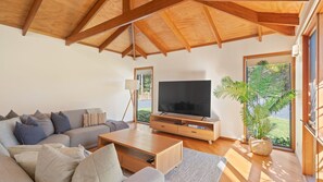 Un salon moderne doté d’un grand téléviseur à écran plat, d’un canapé, d’une table basse et d’une grande fenêtre donnant sur un paysage verdoyant.