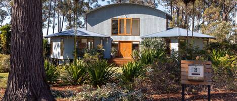 Une maison moderne dotée d’un toit incurvé, entourée d’un jardin où poussent différentes plantes et arbres.