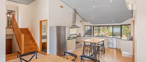 A modern kitchen with a dining area, wooden staircase, and large windows.